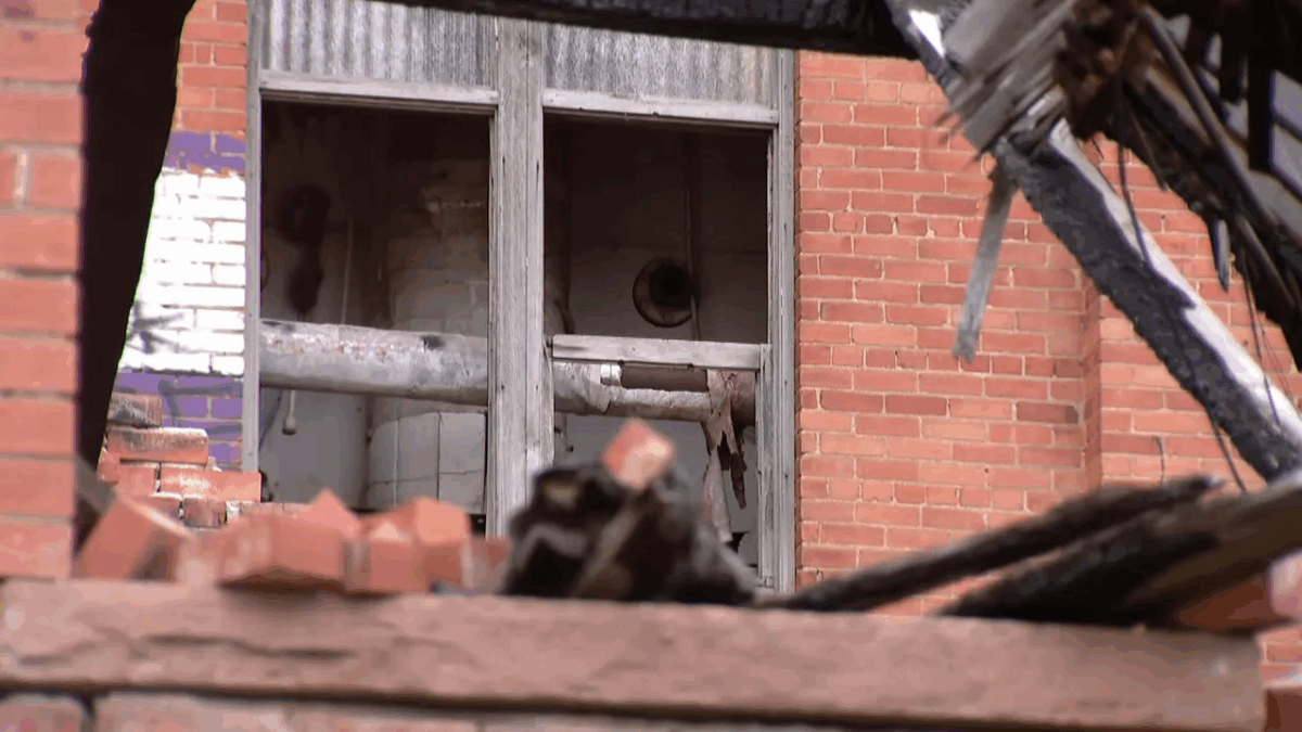 View through collapsed bricks showing damaged interior piping and a broken window in the abandoned sugar mill