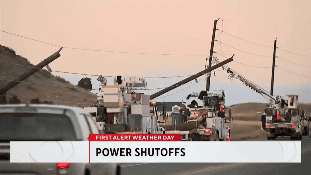 Wide view of utility trucks and leaning/downed power poles on a road as crews respond during power shutoffs