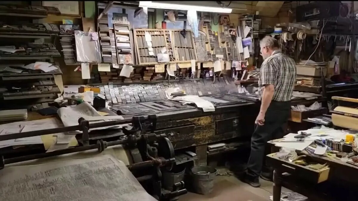 Wide view of a print shop with a large worktable covered in metal type and papers